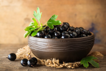 Fresh berries of golden currant in ceramic bowl on wooden background