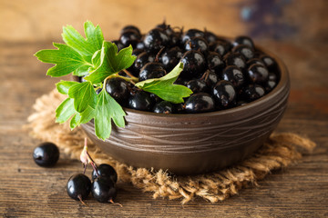 Fresh berries of golden currant in ceramic bowl on wooden background