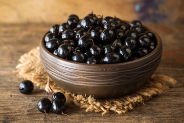 Fresh berries of golden currant in ceramic bowl on wooden background