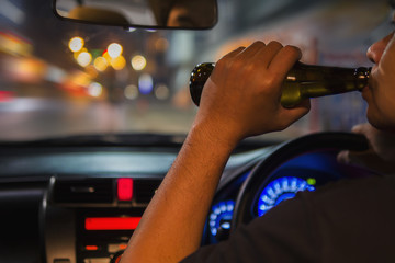 Man drink beer while driving at night in the city dangerously, left hand drive system