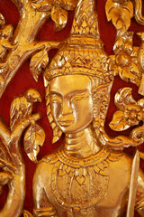 Obraz premium close-up male Thai angel statue filled with gold leaf isolated with red backgrounds, wooden crafting product painted with gold colors, guardian traditional souvenir