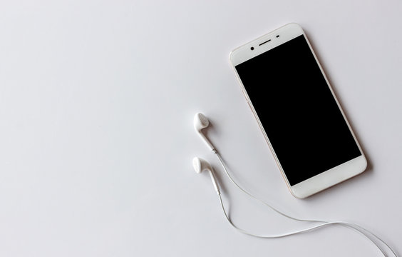 Smartphone And Earphone On White Table With Over Light In The Background