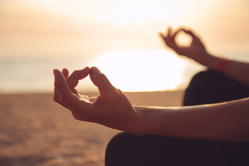 Hands of mature woman practicing yoga at lotus pose, at the sea beach