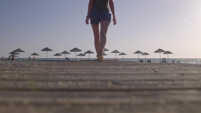 Summer vacation scene. Empty beach with lots of sun umbrella silhouettes on the ocean coast. Fit slim figure of a young beautiful female stranger moving away.