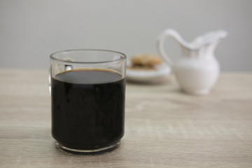 COFFEE MUG AND MILK JAR
Coffee in a transparent cup with milk jar and cookies on the wood table. 