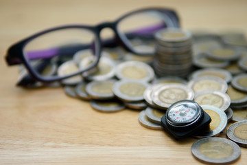 Closeup the compass with blurred coins and glasses on wooden background for financial guide, investor compass, business Growth, money saving planning concept. Selective focus - 169844301