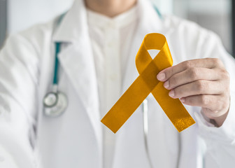 Childhood cancer awareness with gold ribbon symbolic bow color in doctor’s hand