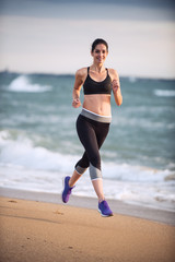 Beautiful young woman in sportswear runs on the beach