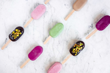Flat lay with colorful popsicles on white marble table. Summer ice cream pattern