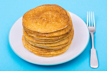 Stack of fresh delicious pancakes on white plate on blue backgro
