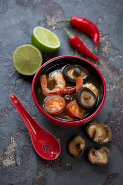 Spicy Thai Tom Yum soup and some of its cooking components on a brown stone background, vertical shot