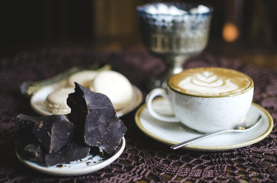 Coffee breack with chocolate and macaroons. Latte on retro brown wooden table with tablecloth