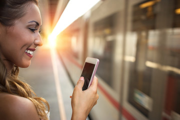 Beautiful young woman looking into her smartphone at a train station