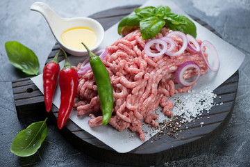 Raw fresh pork mincemeat with chili peppers, green basil leaves, onion, olive oil and sea salt, horizontal shot