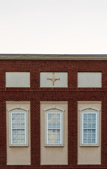 Historic brick facade of a building with three windows and decorative four pointed relief sculpture on the upper center part of the building
