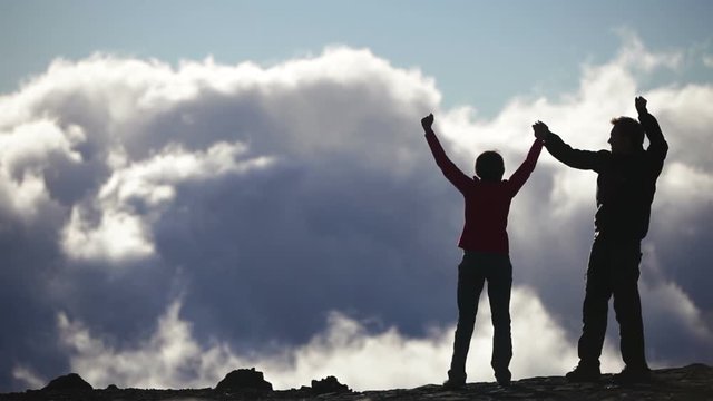 Achievement, Success and accomplishment high five concept with hiking people cheering and celebrating of joy with arms raised outstretched up above the clouds on trekking hike. Woman and man Hikers.