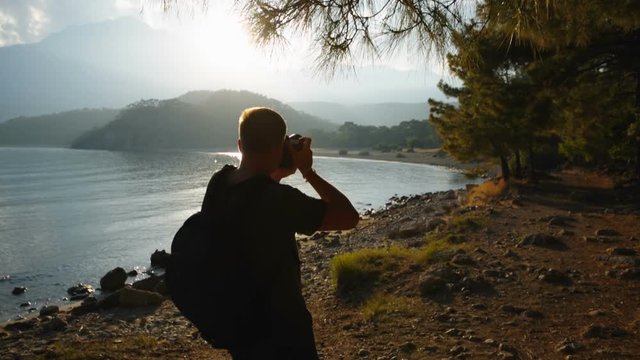 traveler photographer shoots beautiful sunset on the shore of a mountain lake