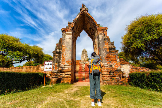 Young asian female traveler with backpack traveling with standing look at view with old temple (Wat Mahathat), Ayutthaya Province, Thailand