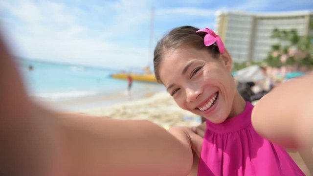 Selfie beach travel woman self portrait video smiling happy and joyful to camera. Multiracial Caucasian Asian girl on Waikiki beach in Honolulu, Oahu, Hawaii, USA.