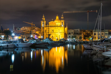 The beautiful Msida Parish Church at deep night with harbor at the foreground. Malta.