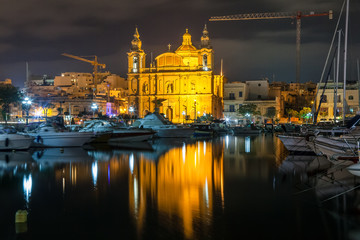 The beautiful Msida Parish Church at deep night with harbor at the foreground. Malta.