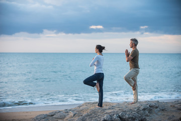Beautiful couple practicing yoga on the beach at sunrise