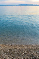 Obraz premium Calm clean sea with pebble beach and land on the horizon.