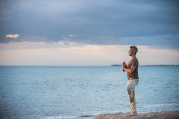  gray-haired man practicing yoga on the beach at sunrise