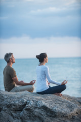 Fototapeta premium Couple practicing yoga at sunrise on the beach facing the sea