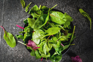 Bowl with fresh green organic leaves, baby spinach lettuce, on a black stone table, copy space top...