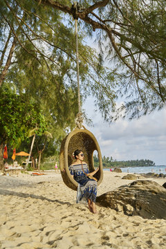 Woman sits in hanging basket chair on beach