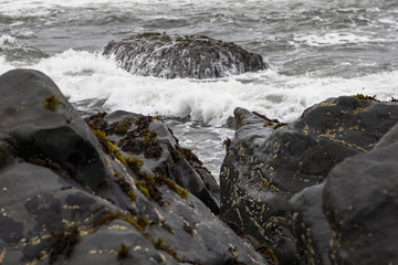 Waves crashing over black shoreline rocks at high tide