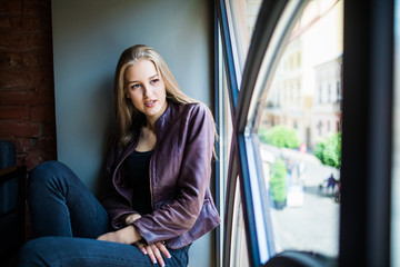 Young woman is sitting on a window sill in a cafe and enjoy free time