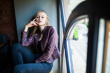 Young woman is sitting on a window sill in a cafe and enjoy free time