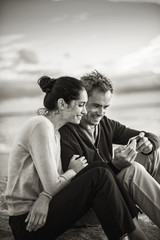 A couple sitting at the beach, looking at photos on a phone