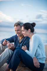 A couple sitting at the beach, looking at photos on a phone