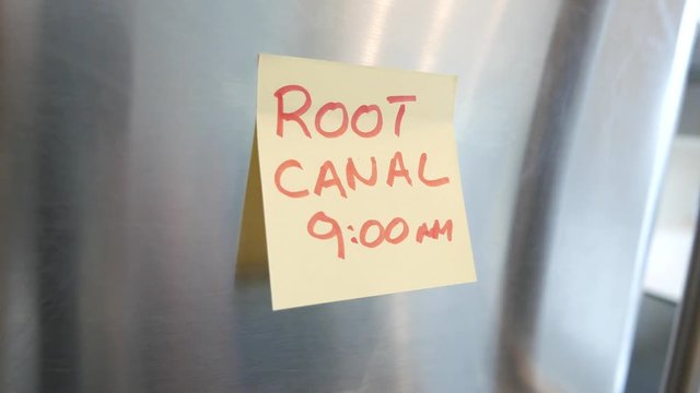 Putting a Root canal sticky note reminder on a fridge. Closeup on the hand and paper.