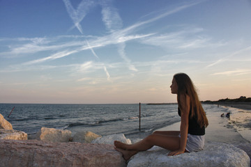 GIOVANE RAGAZZA SEDUTA SUGLI SCOGLI AL MARE