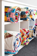 Fototapeta premium patchwork, sewing and fashion concept - white bookcase with six shelves and bright finished quilts in the studio, the warehouse of finished products, side view, vertical