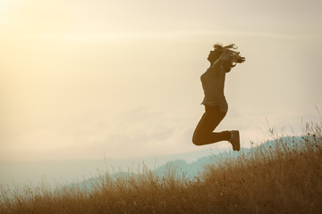 Girl jumping on mountain and having fun on idyllic field at sunset