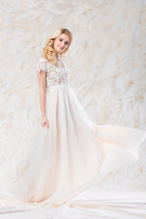 Fototapeta na wymiar fashionable wedding dress, beautiful blonde model, bride hairstyle and makeup concept - stunning young woman in luxury long white gown indoors on light background, happy female posing with a smile