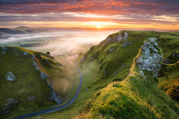 Fototapeta premium Długa kręta wiejska droga prowadząca do mglistej doliny w angielskim Peak District.