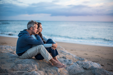Beautiful couple sitting at the beach watching the sunset - Powered by Adobe