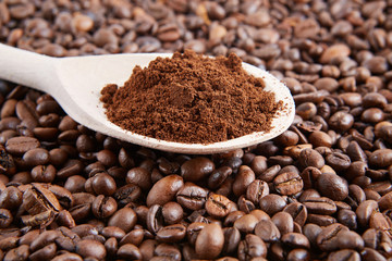 Wooden spoon with ground coffee on the background of the beans. 