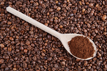 Wooden spoon with ground coffee on the background of the beans.