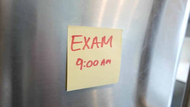 Putting a Exam sticky note reminder on a fridge. Closeup on the hand and paper.