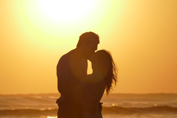 Aoung couple is kissing at beach during sunset - obrazy, fototapety, plakaty