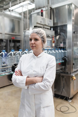 Young happy woman worker checking robotic line for bottling and packaging pure drinking water into bottles and canisters.