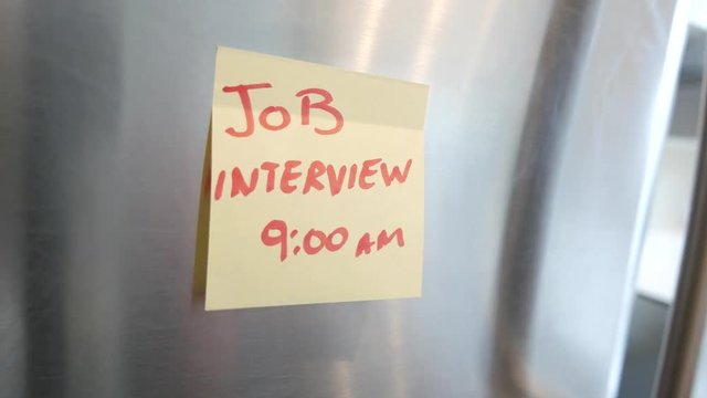 Putting a Job Interview sticky note reminder on a fridge. Closeup on the hand and paper.