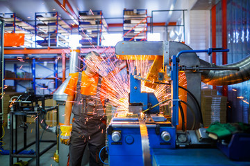 A male mechanic working on welding machine in the Industrial production of metal products. Sparks...